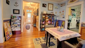 Ein gemütliches Zimmer mit Holzboden, einem Esstisch mit Tischdecke, einem Bücherregal und einer Pinnwand mit verschiedenen Mitteilungen.