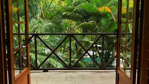 An open wooden door leading to a balcony with a view of lush greenery and a hanging lantern.