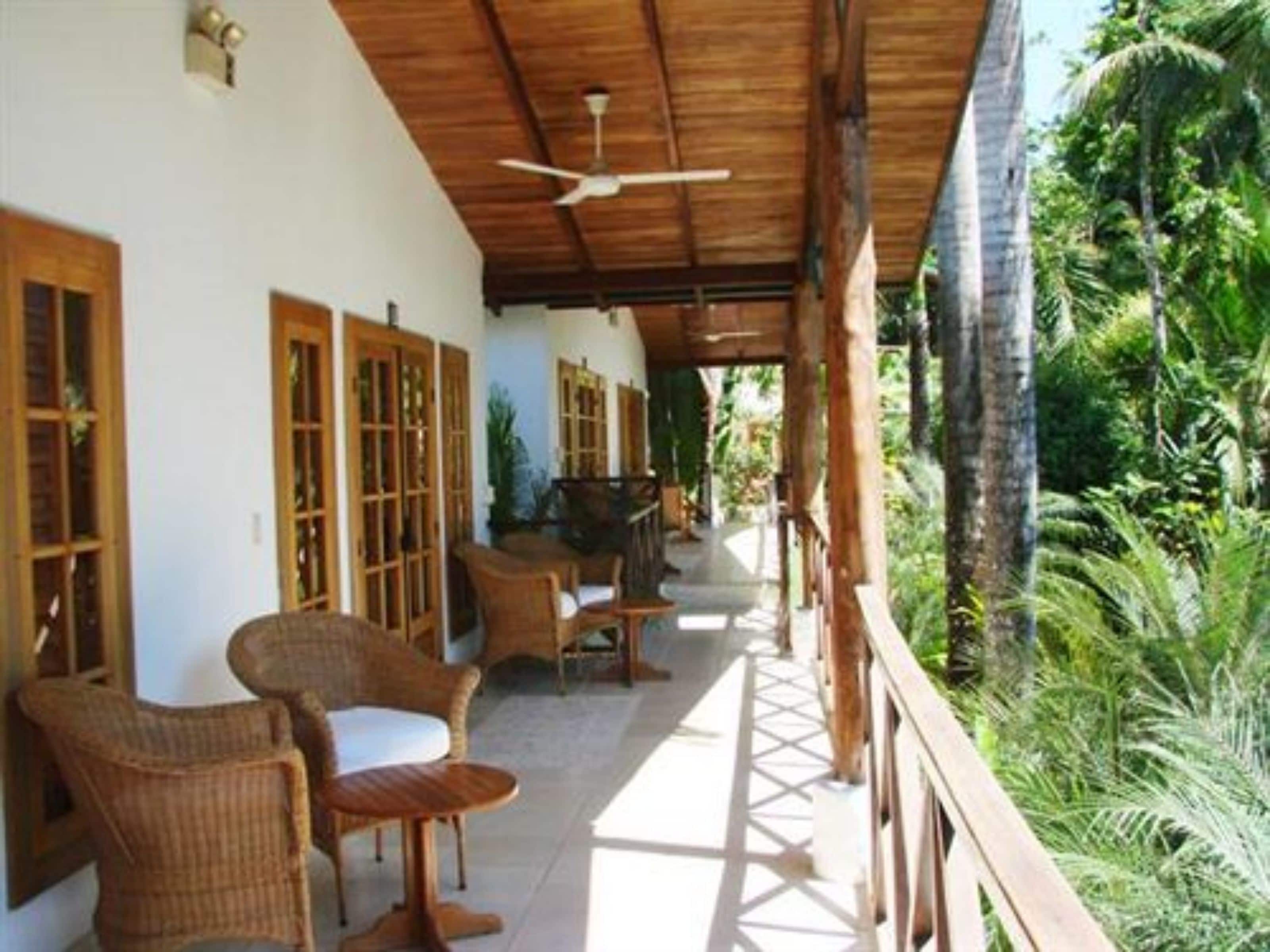 A covered outdoor seating area with wicker furniture, wooden doors, and a ceiling fan.