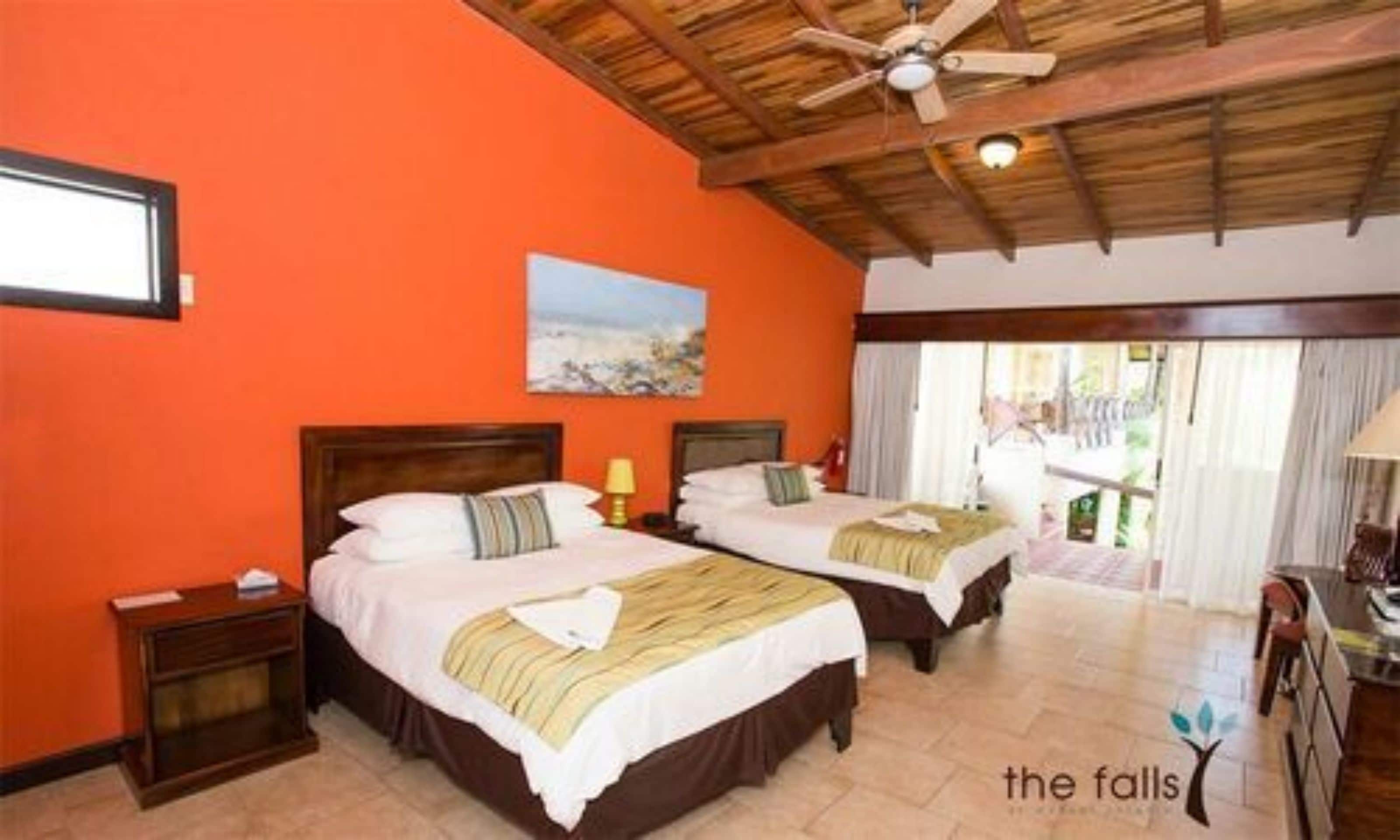 Habitación de hotel con dos camas, ventilador de techo y un cuadro en la pared.