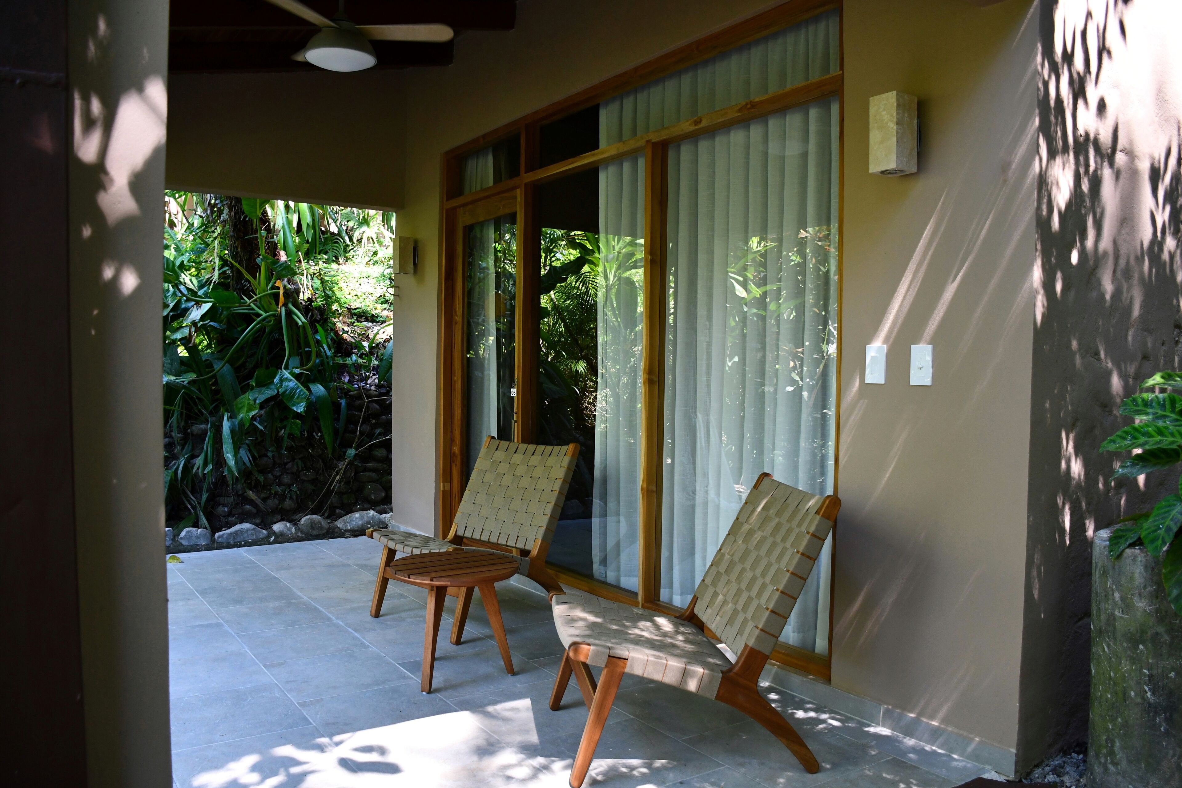 A patio with two wooden chairs and a table, a sliding glass door, and a view of greenery outside.