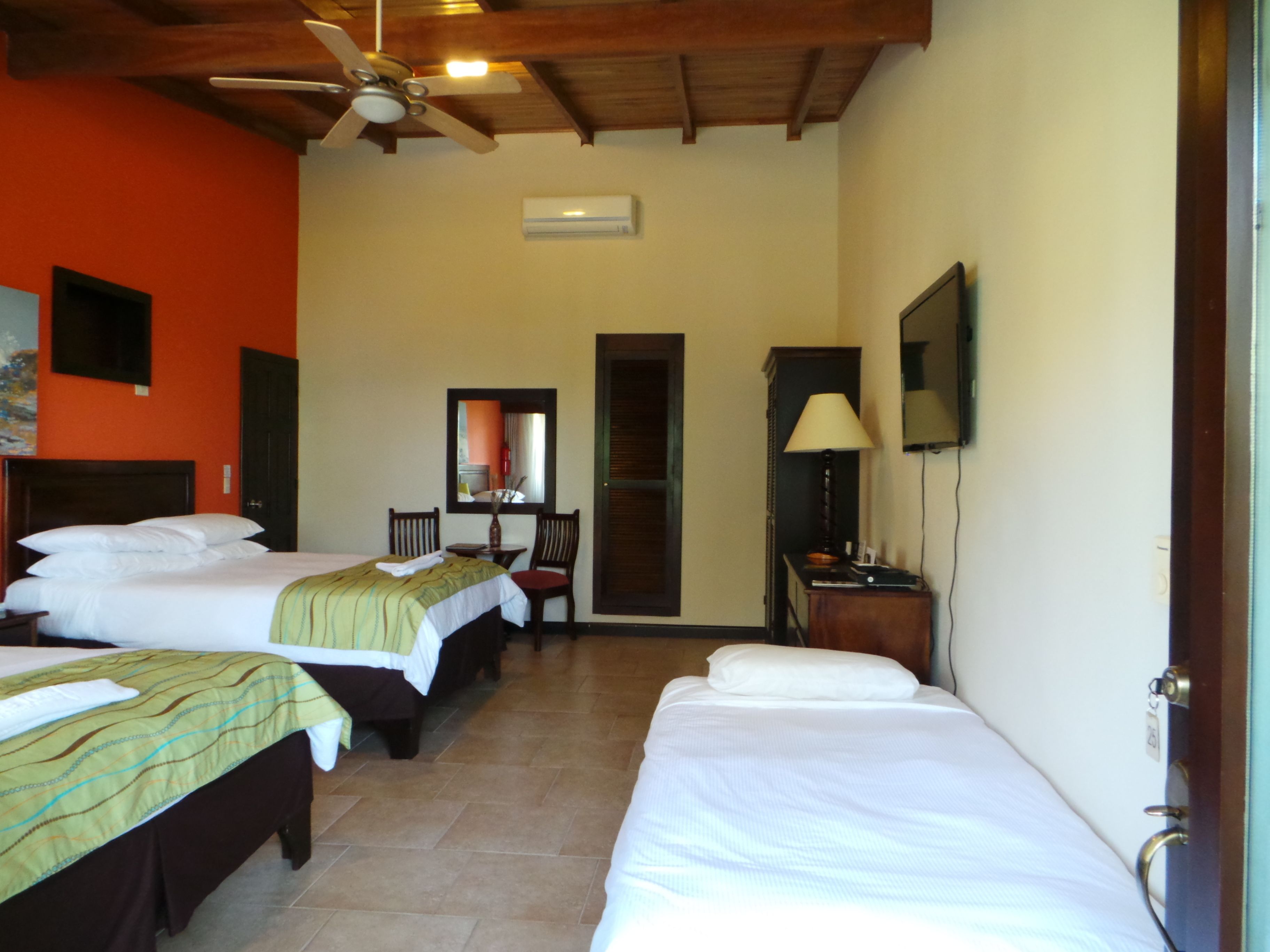 Habitación de hotel con dos camas, ventilador de techo, televisor y puerta.