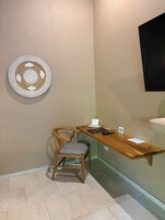 Una habitación pequeña con un escritorio de madera, una silla, un televisor montado en la pared y un adorno colgando de la pared.