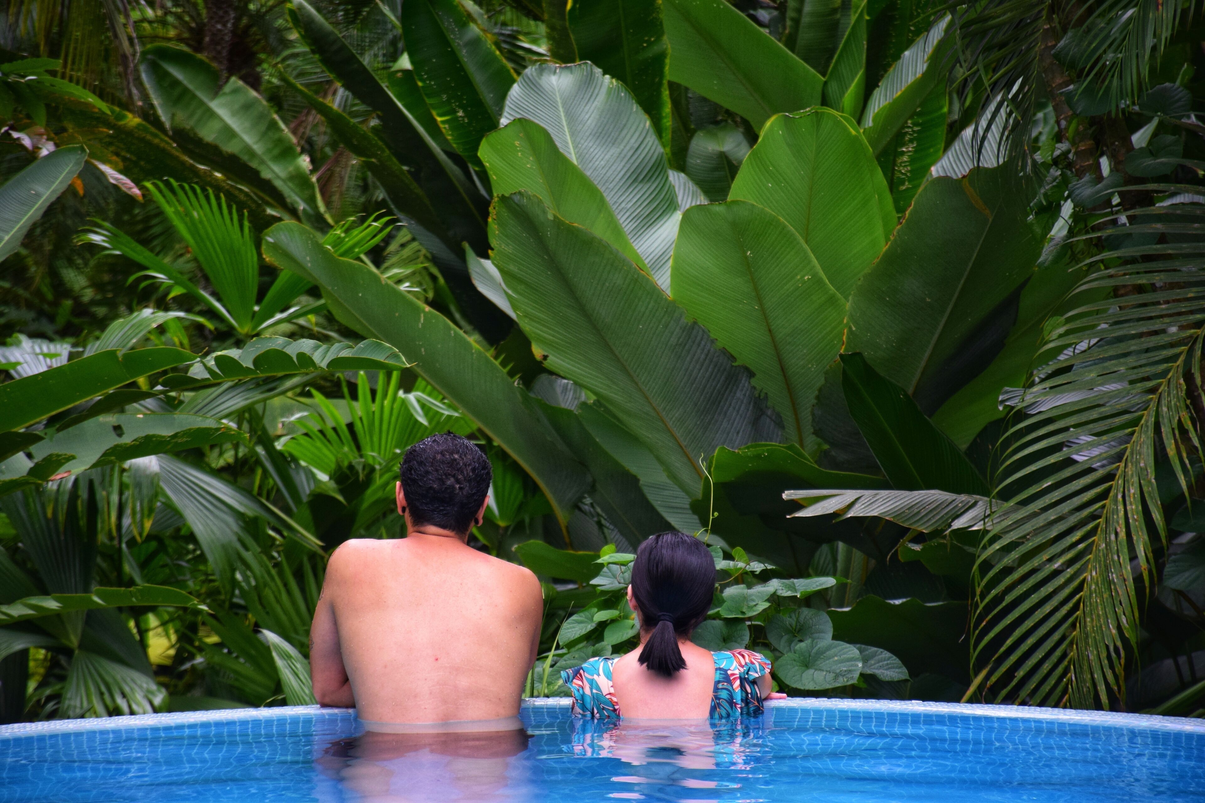 A couple in a swimming pool surrounded by lush tropical foliage.