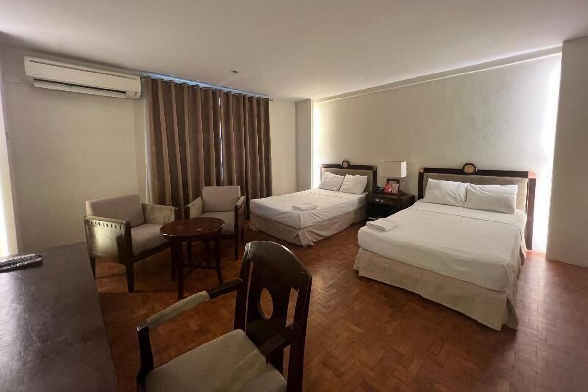 Habitación de hotel con dos camas, un escritorio, una silla y una mesita.