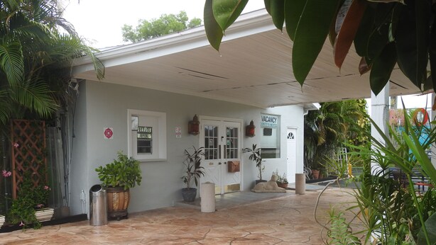 A hotel entrance with a covered patio, potted plants, and a sign indicating the office is open.