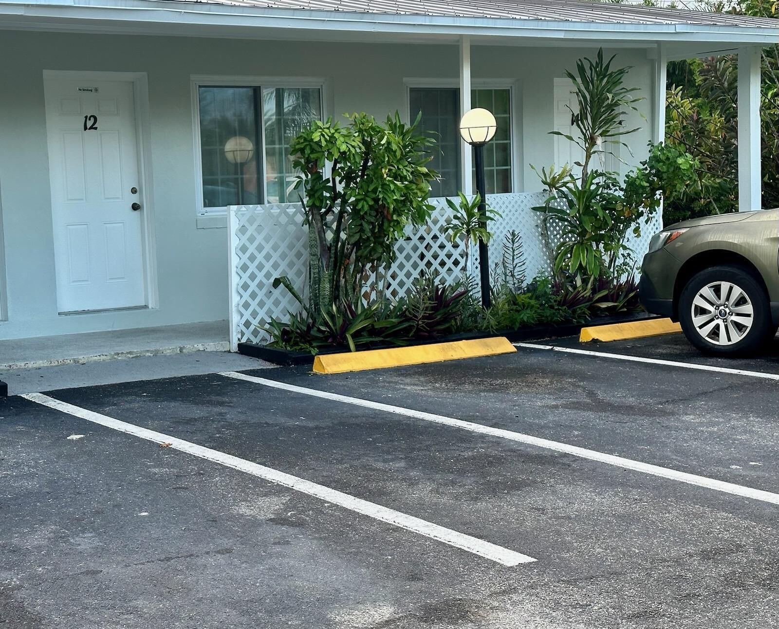 A parking lot with a white building, a door labeled '12', and a parked car.