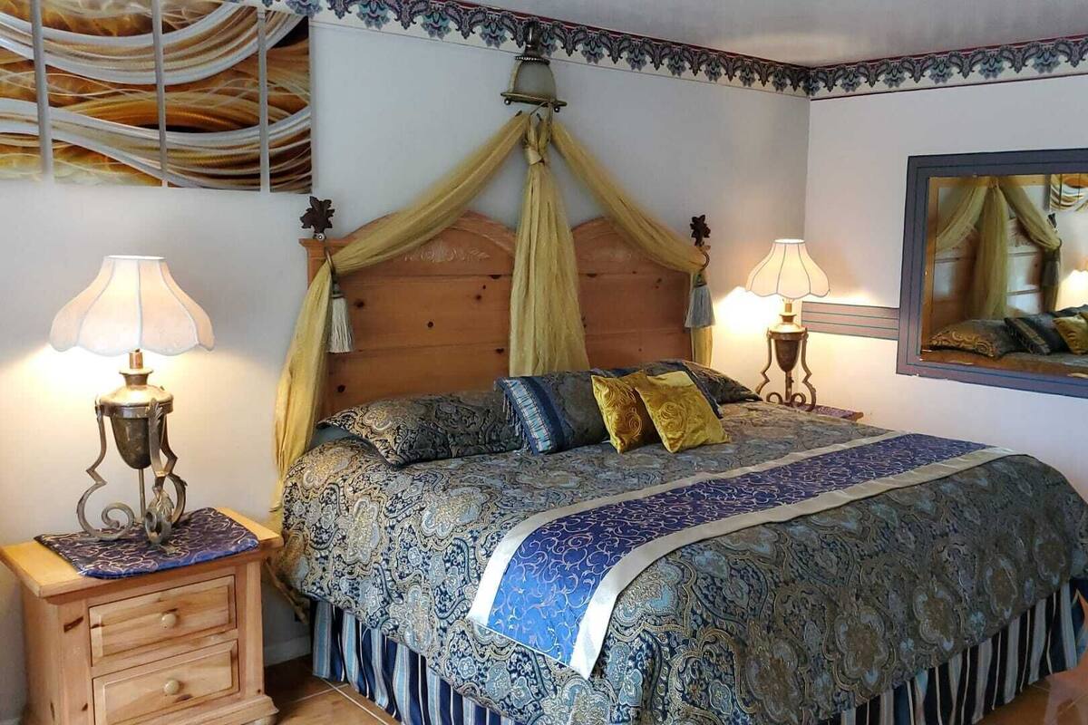 A bedroom with a canopy bed, two bedside lamps, a wooden nightstand, and a mirror on the wall.