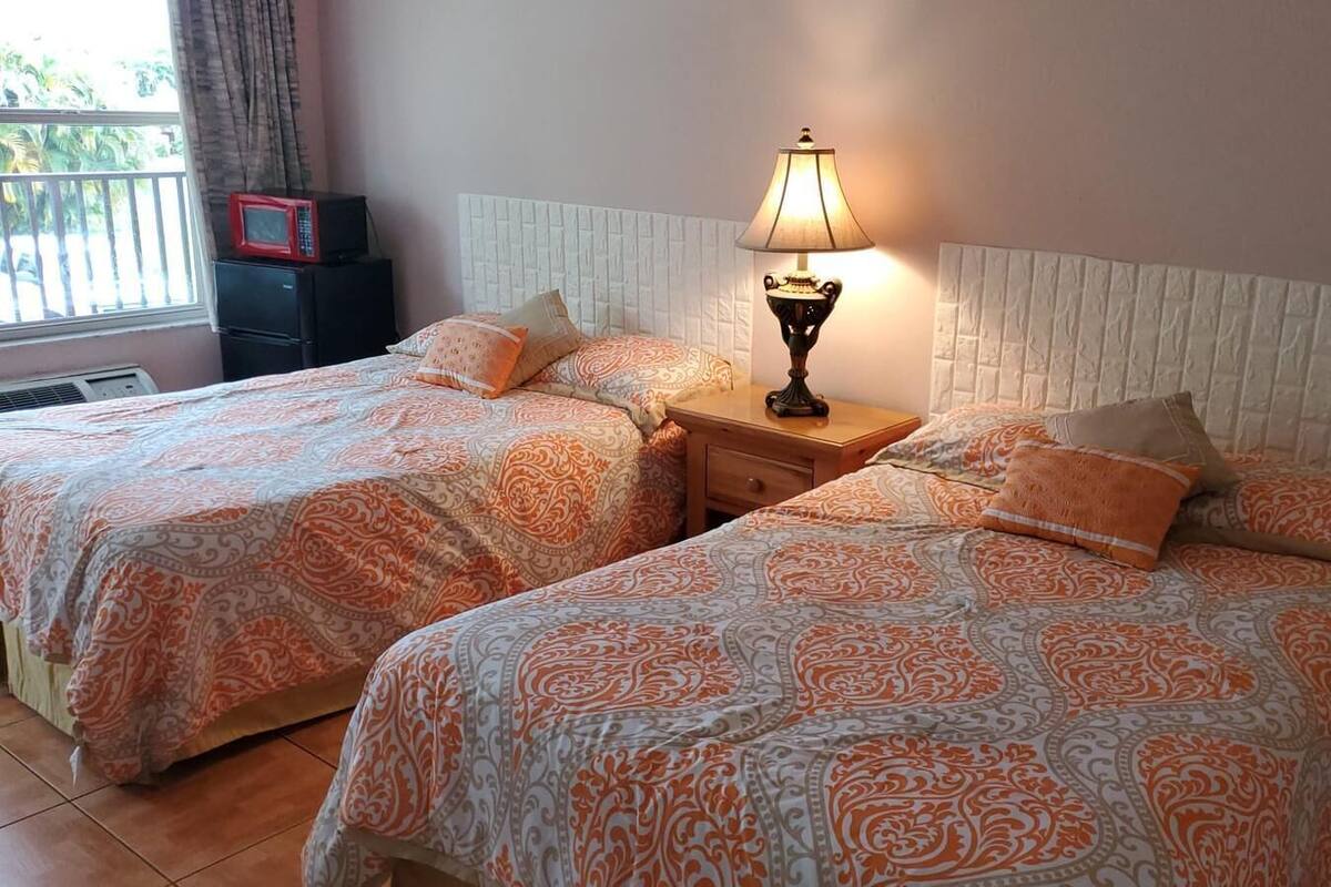 A room with two beds, each with patterned bedding, a bedside lamp, and a small table.