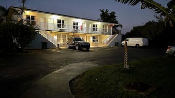 Un motel à deux étages, doté d’un balcon à l’étage supérieur, d’un espace de stationnement et d’un SUV noir garé devant.