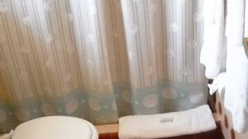 A bathroom with a toilet, a shower curtain with a scalloped edge, and a tiled floor.