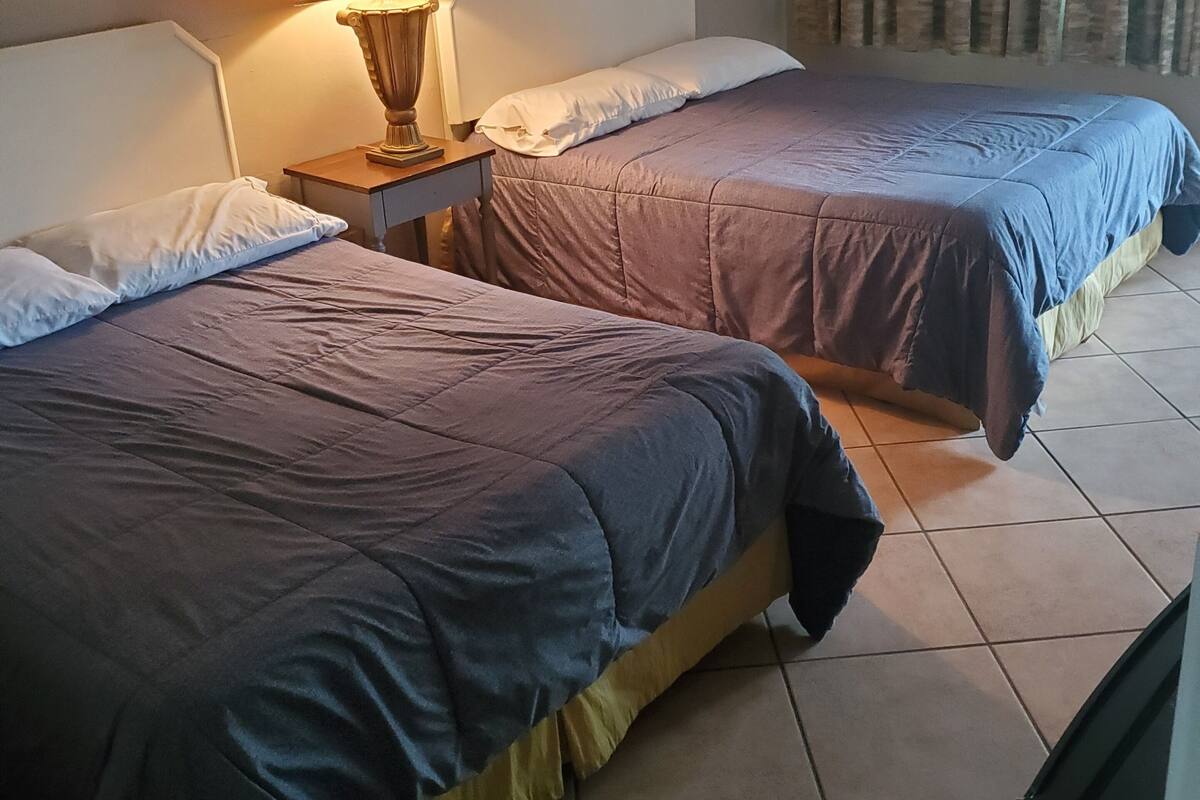 A hotel room with two beds, a nightstand with a lamp, and a curtain.