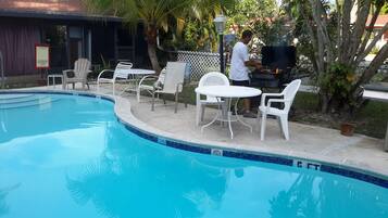A swimming pool with white chairs and a grill area.