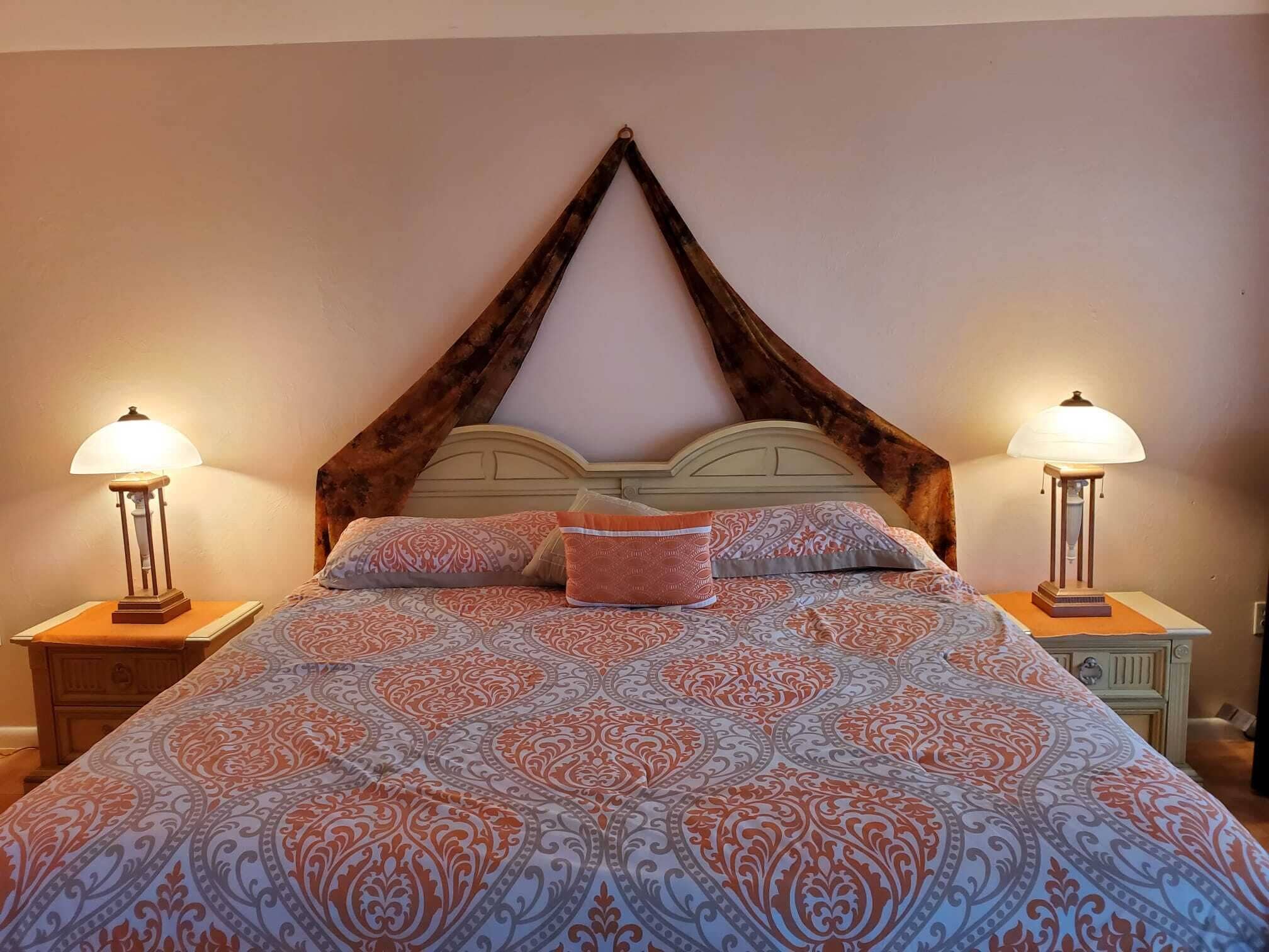 Ein Bett mit einem gemusterten Bettüberwurf, zwei Nachttischlampen und einem hölzernen Kopfteil.