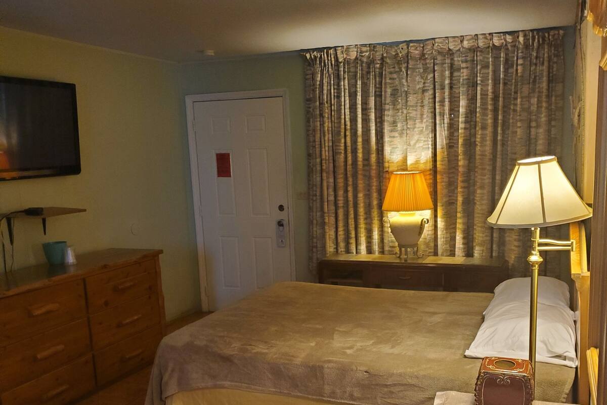 A hotel room with a bed, a dresser, a television, and a lamp.