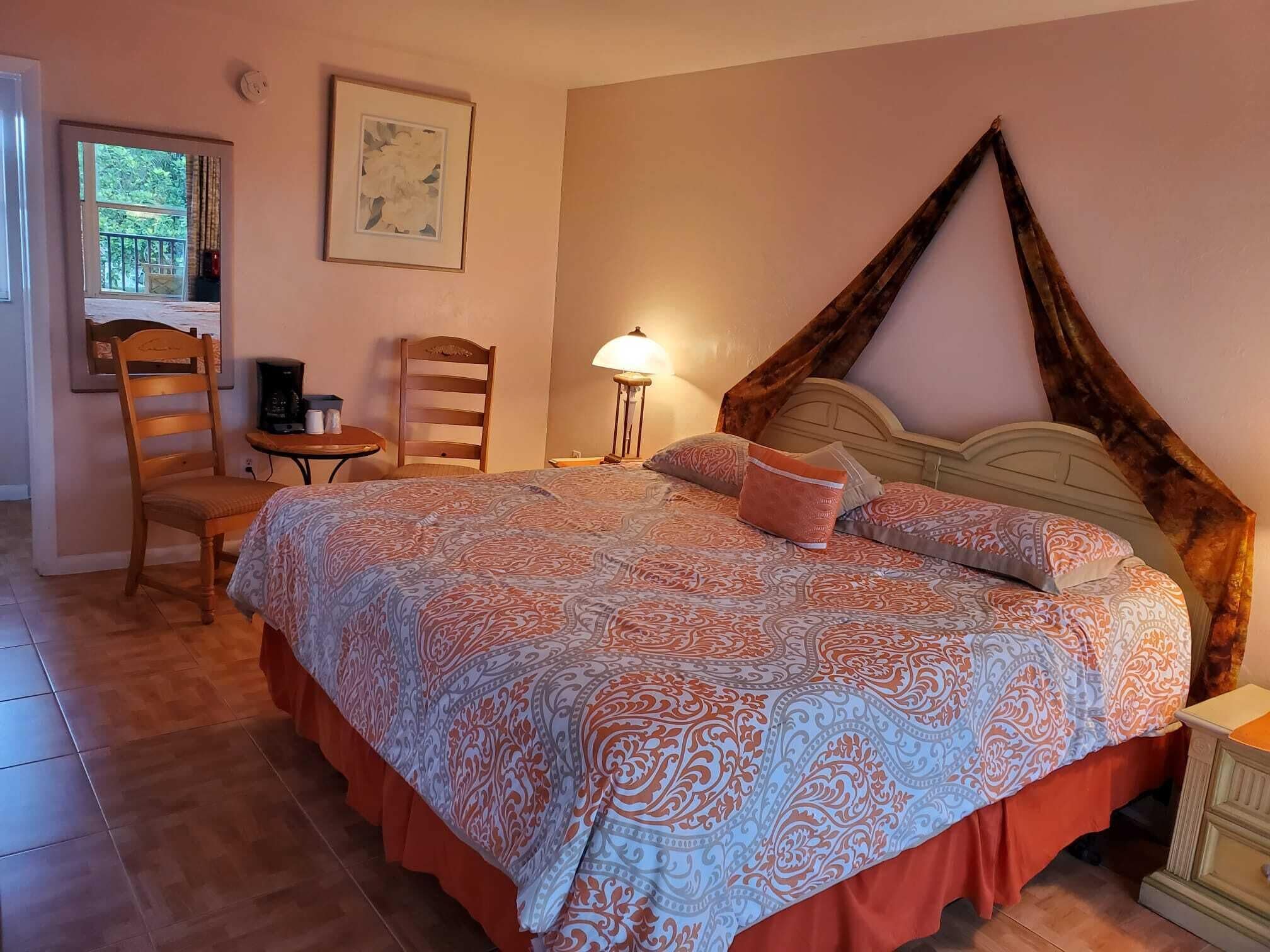 A bedroom with a large bed, a chair, a small table, a lamp, and a painting on the wall.