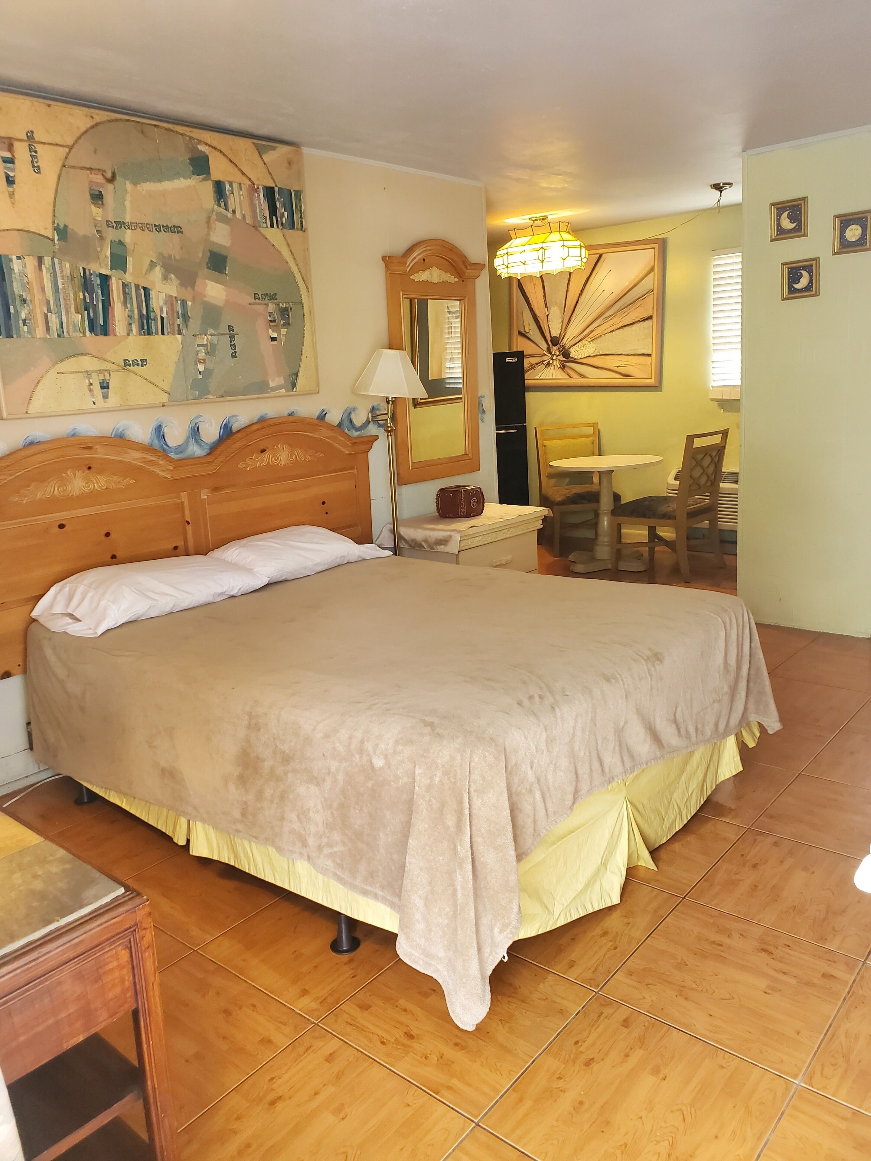 Een slaapkamer met een groot bed, een houten hoofdbord, een nachtkastje, een lamp, een stoel, een klein tafeltje en een wandklok.