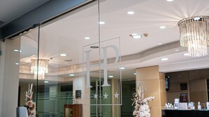 A hotel reception area with a glass partition displaying the logo 'HP'. There are chandeliers, a reception desk, and a floral arrangement. - Hotel Première Pool & Resort (Giugliano in Campania)