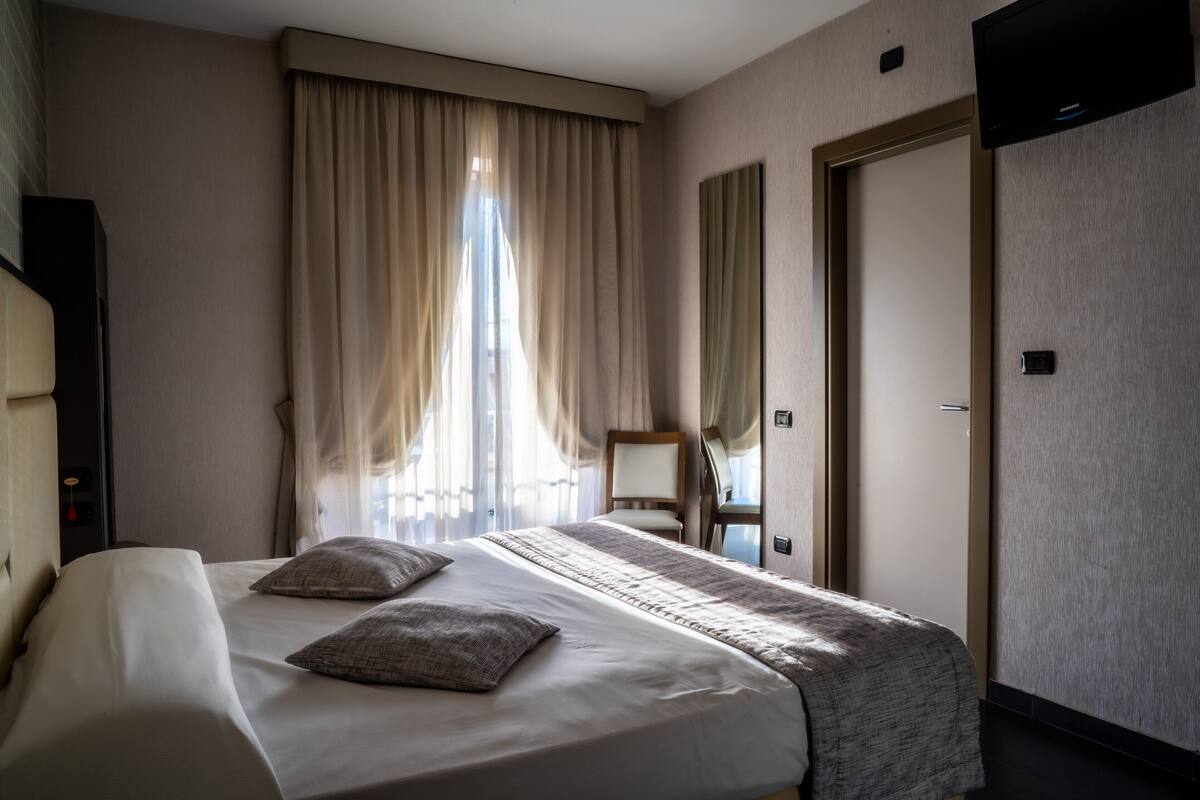 A hotel room with a large bed, a chair, a desk, and a television on the wall.