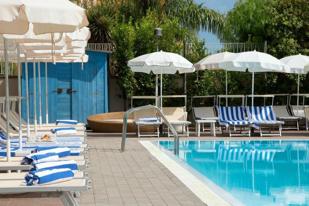 A pool area with lounge chairs and umbrellas, a blue door, and a tiled floor.