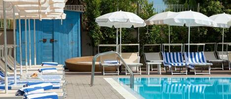 A pool area with lounge chairs and umbrellas, a blue door, and a tiled floor.