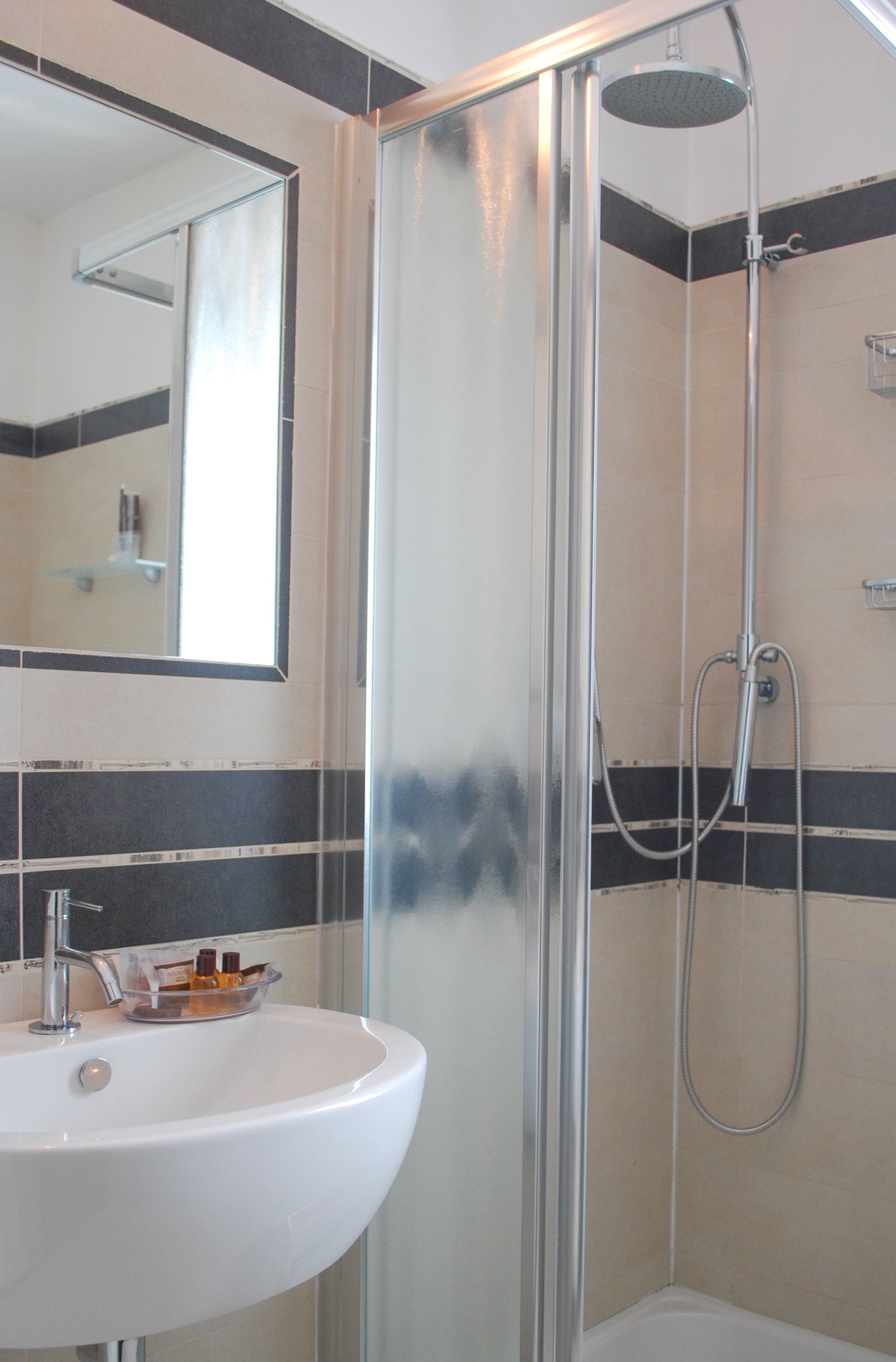 Une salle de bain avec une douche à parois de verre, un lavabo blanc avec des articles de toilette et un miroir au-dessus du lavabo.