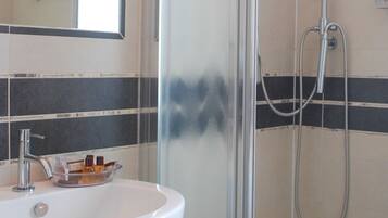 Une salle de bain avec une douche à parois de verre, un lavabo blanc avec des articles de toilette et un miroir au-dessus du lavabo.