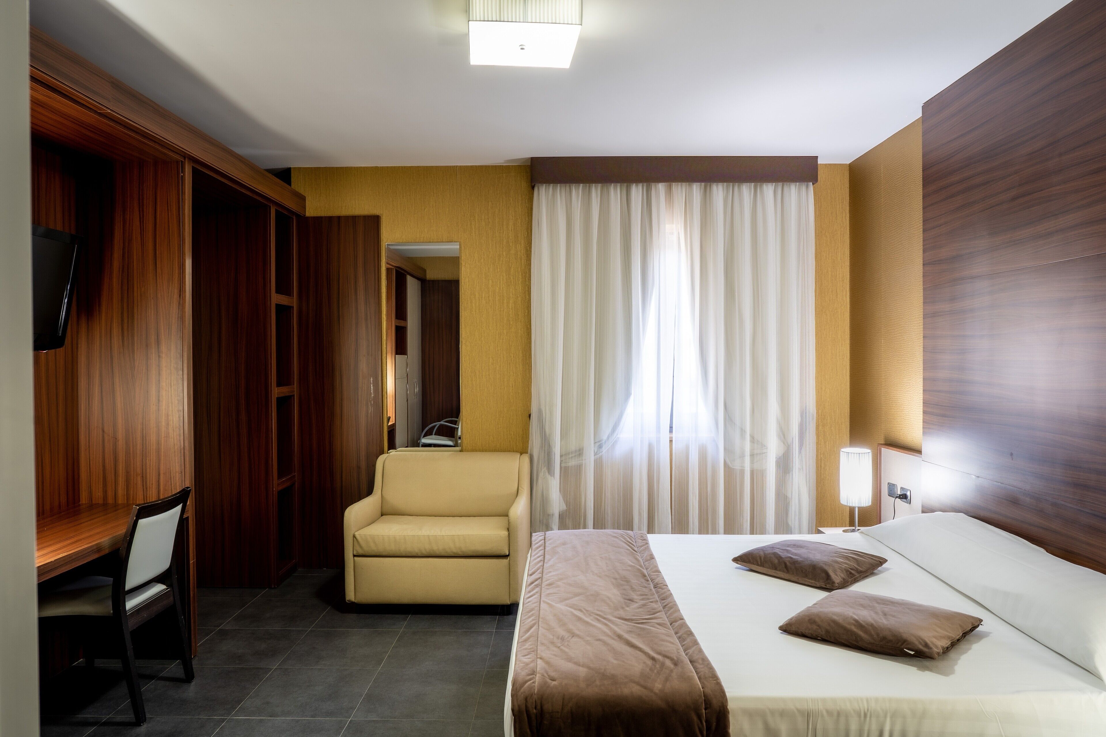 A hotel room with a bed, a desk, a chair, a wardrobe, and a television.