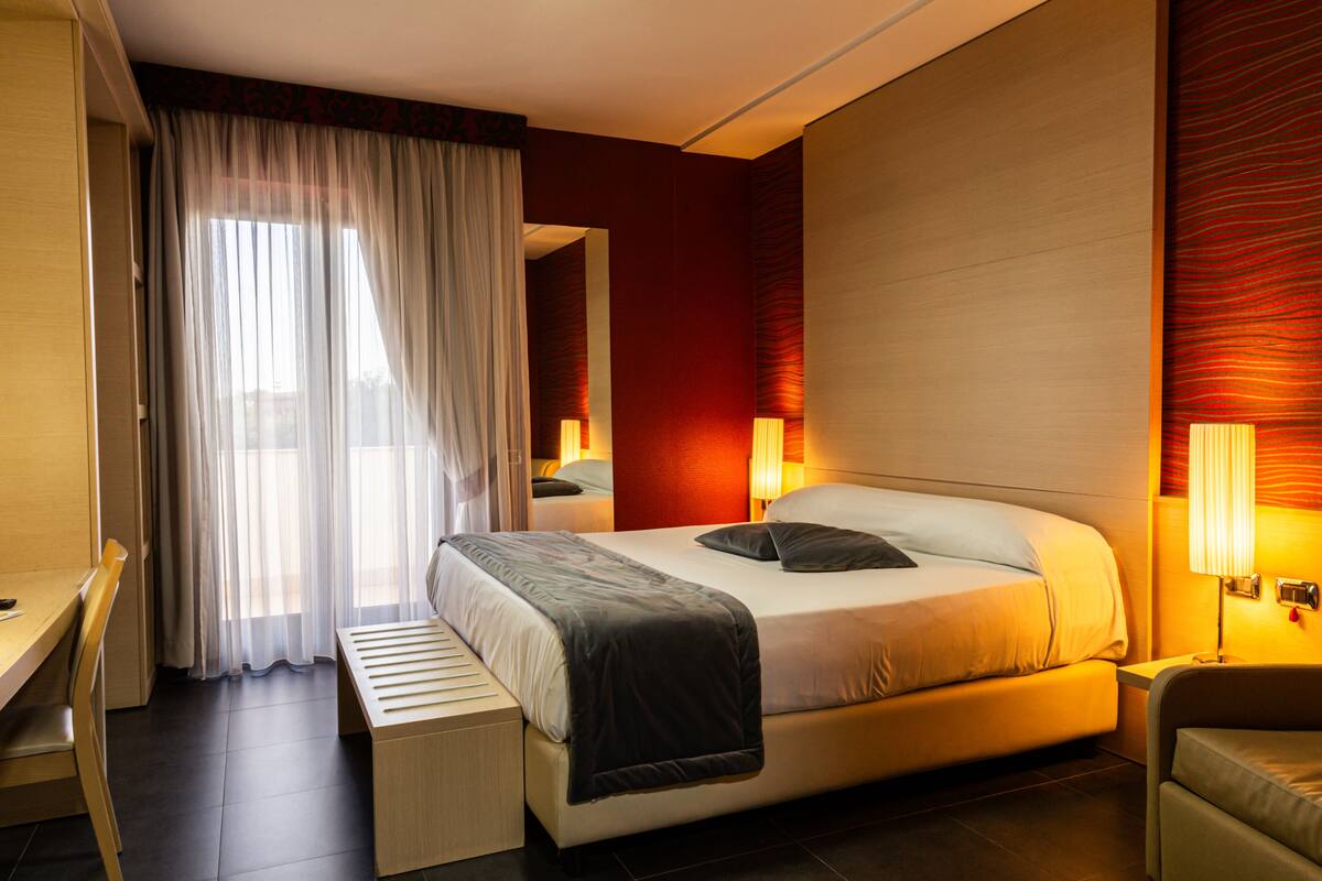 A modern hotel room with a large bed, bedside lamps, a desk, and a view of the outdoors.