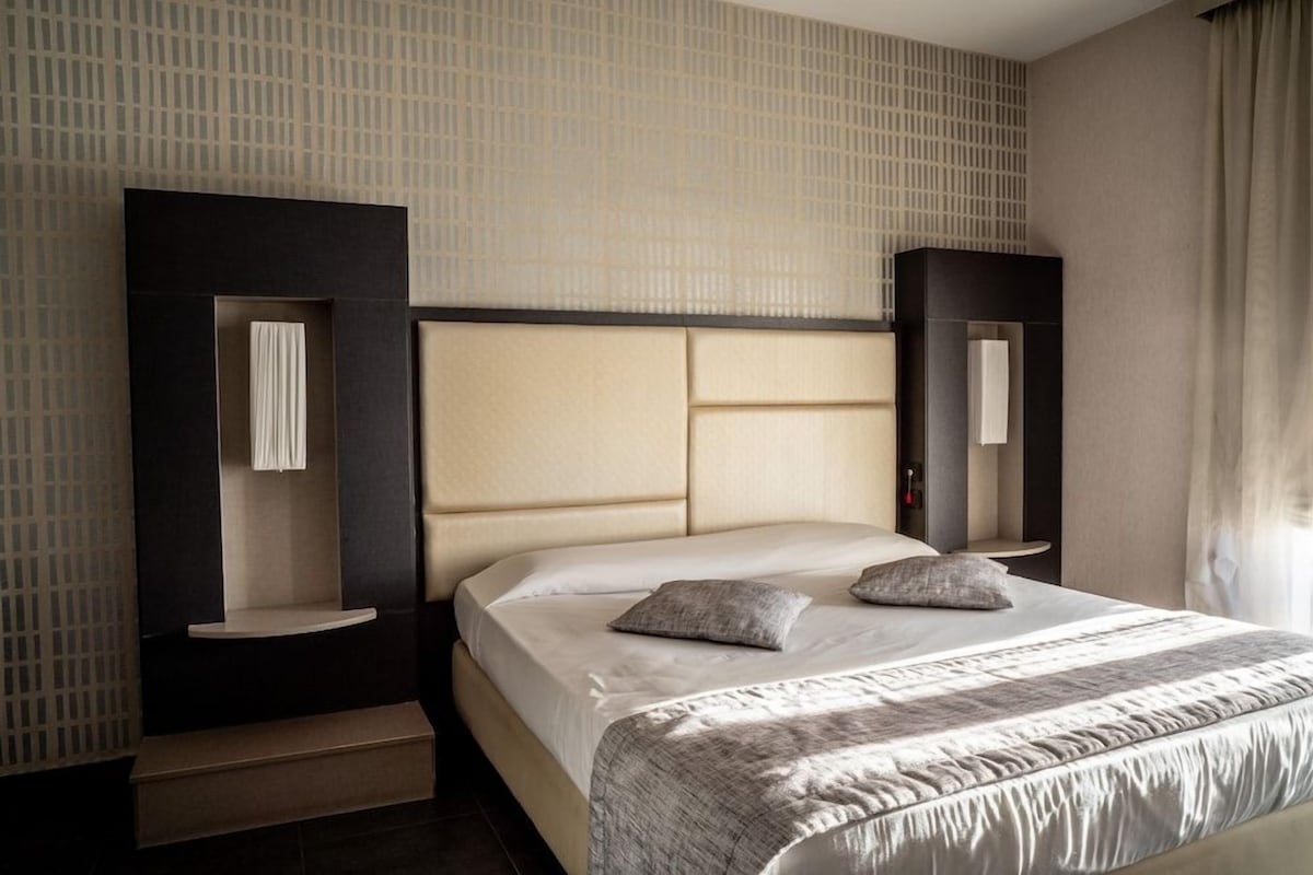 A modern hotel room with a large bed, built-in shelving, and a large mirror.