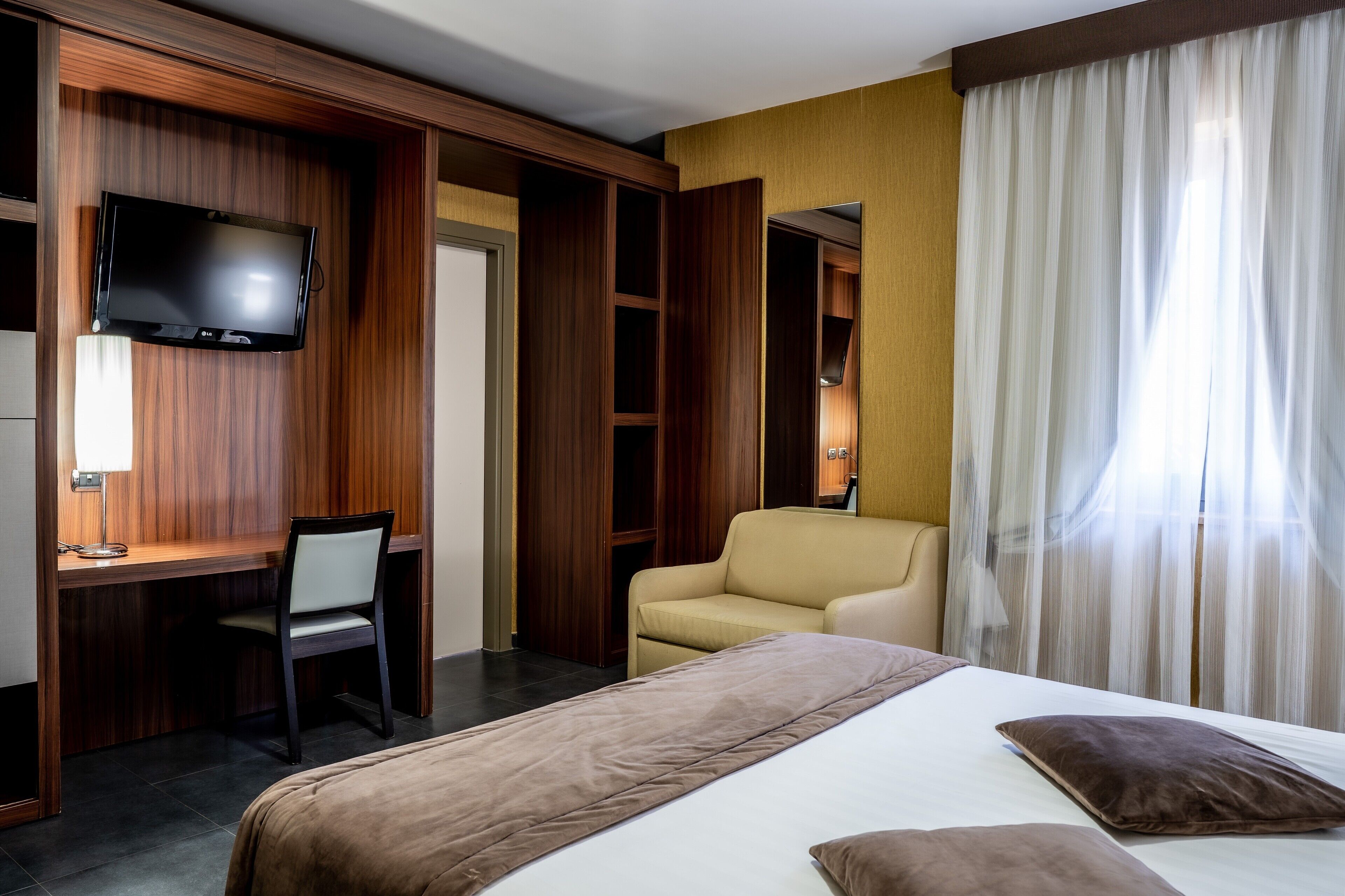 A hotel room with a bed, a desk, a chair, a television, and a wardrobe.