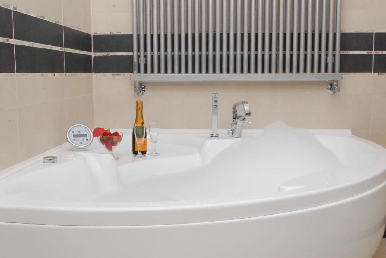 A white bathtub with a digital water temperature control, a champagne bottle, and a glass.