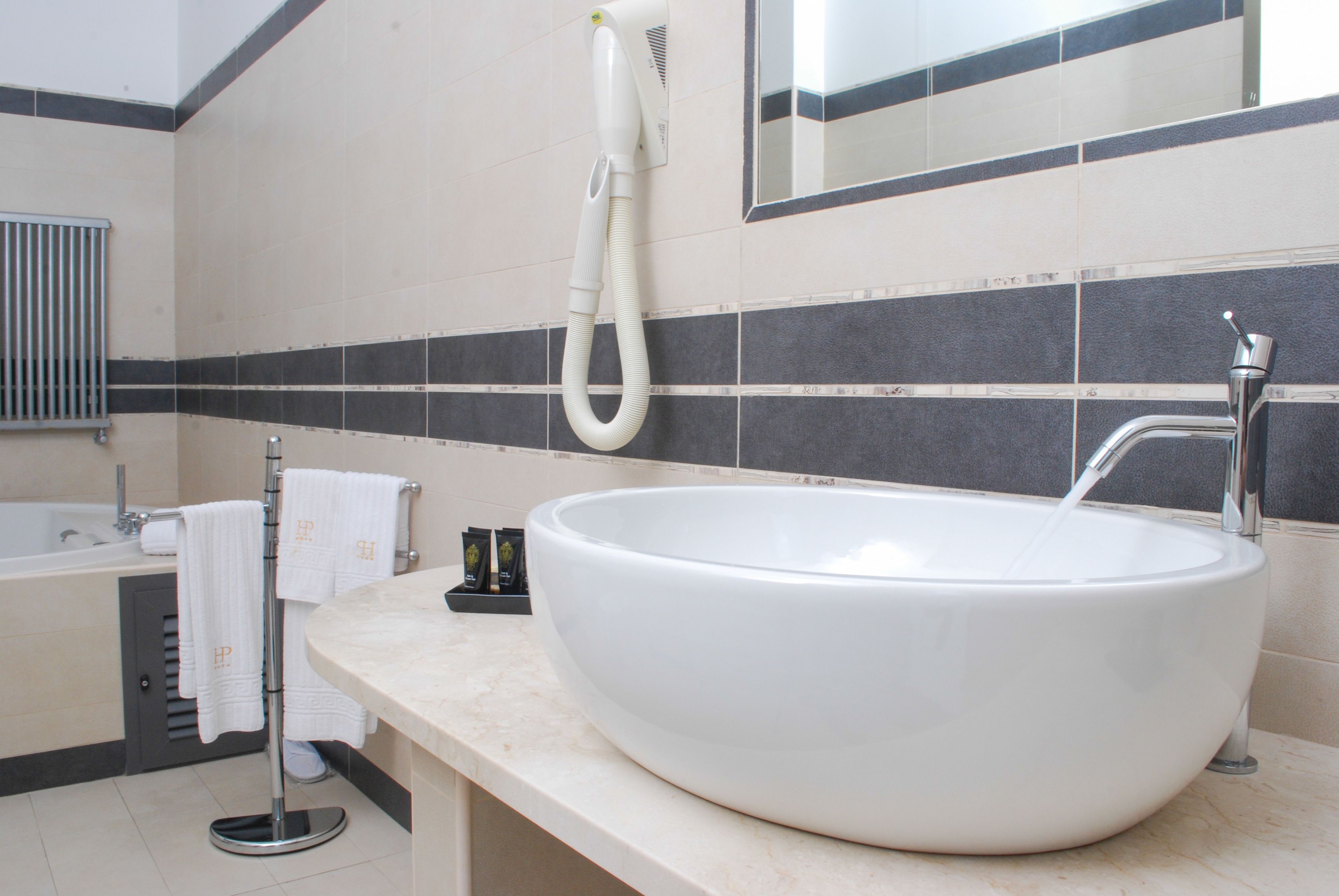 A large white sink with a modern faucet, a towel rack with white towels, and a hairdryer on a wall-mounted stand.