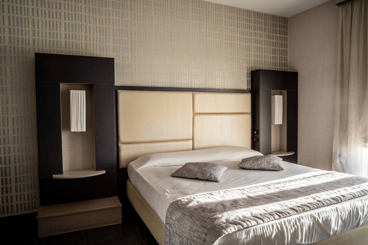 A modern hotel room with a large bed, built-in shelving, and a large mirror.
