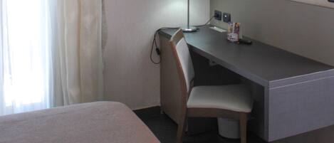 Habitació d'hotel amb llit, escriptori amb cadira, làmpada, televisió i finestra amb cortines.
