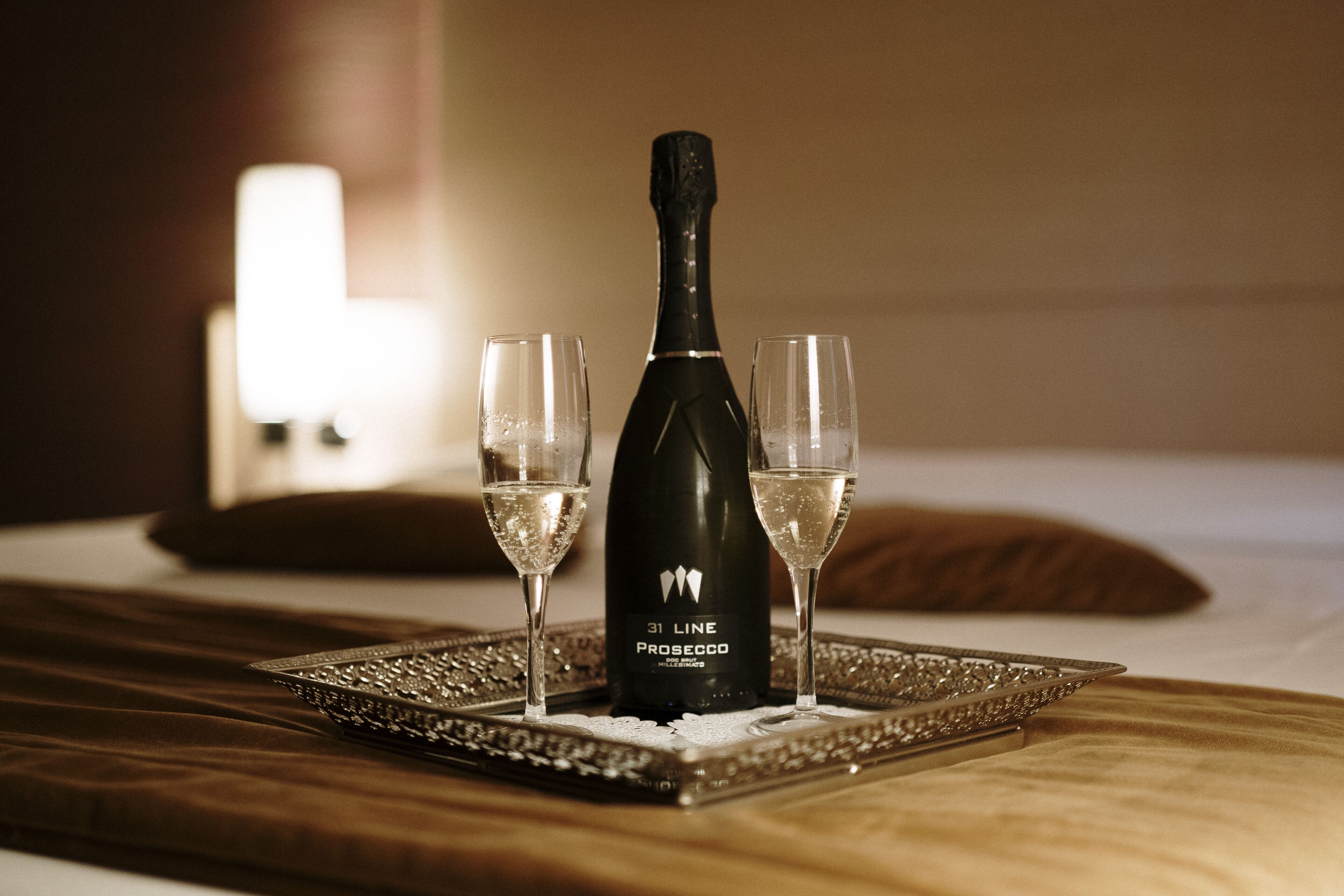 Una botella de Prosecco 31 Line sobre una bandeja con dos copas de champán sobre una cama.
