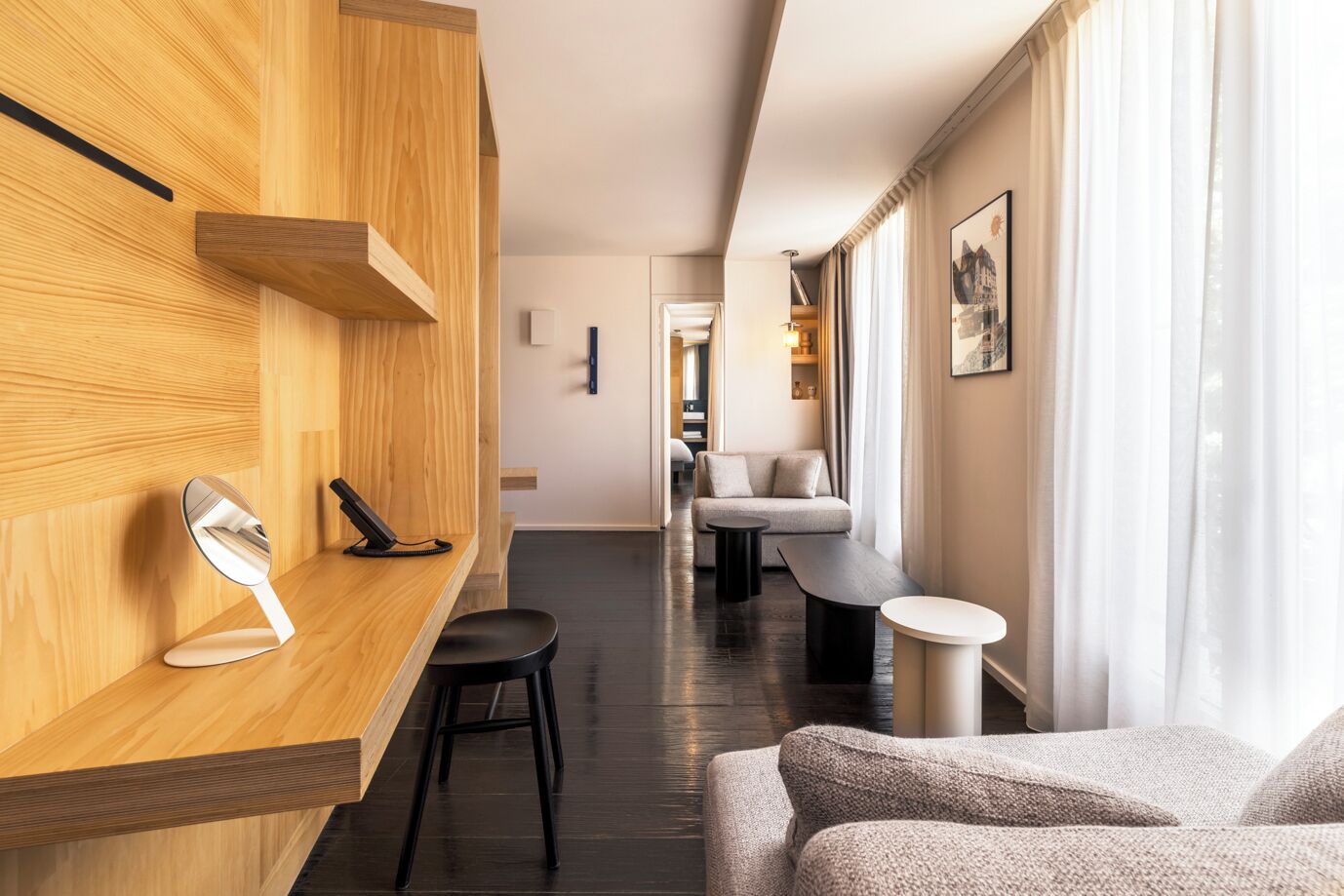 A modern hotel lobby with a wooden reception desk, a mirror, a black telephone, a sofa, and a small table.