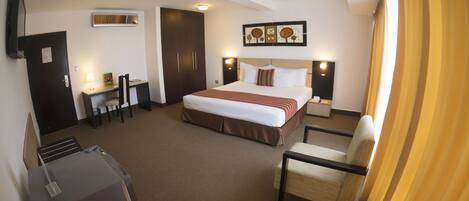 A hotel room with a bed, desk, chair, and a TV on the wall.