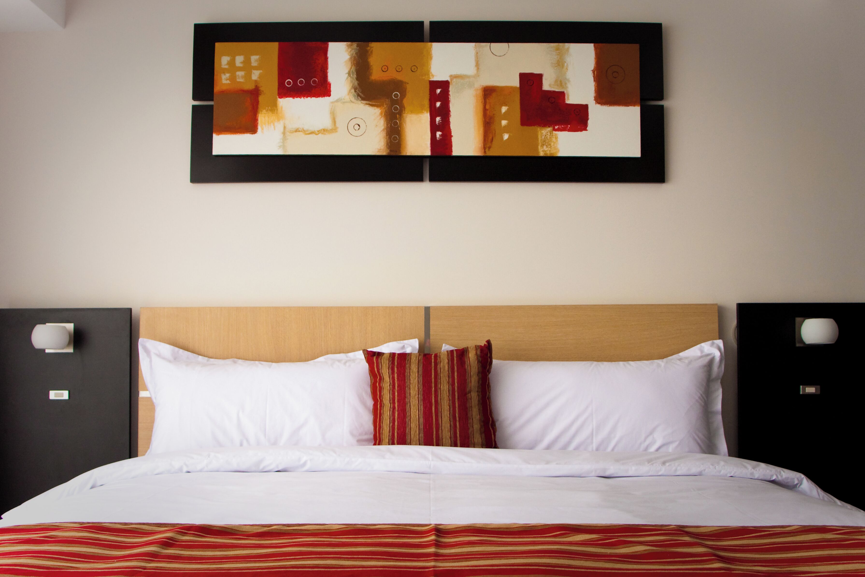 A hotel room with a large bed, two bedside tables, a headboard, and a wall-mounted abstract art piece.