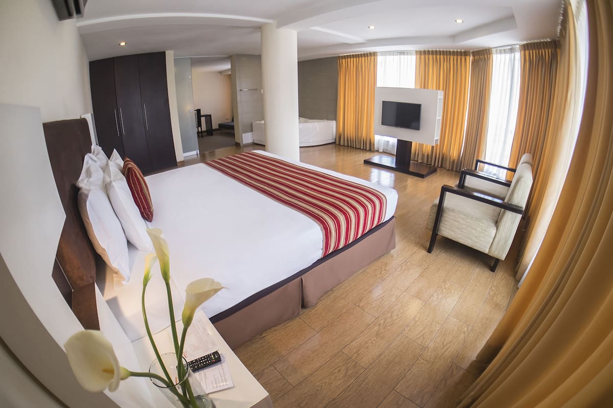 A hotel room with a large bed, a TV, a chair, and a desk with a remote control.