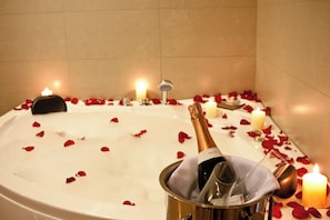 Ett badkar fyllt med vatten, omgivet av rosenblad och ljus, med en flaska champagne i en hink.