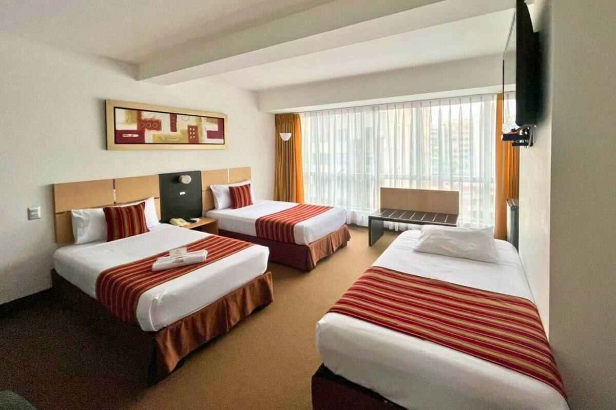 A hotel room with two beds, a desk, a chair, a TV, and a window with curtains.
