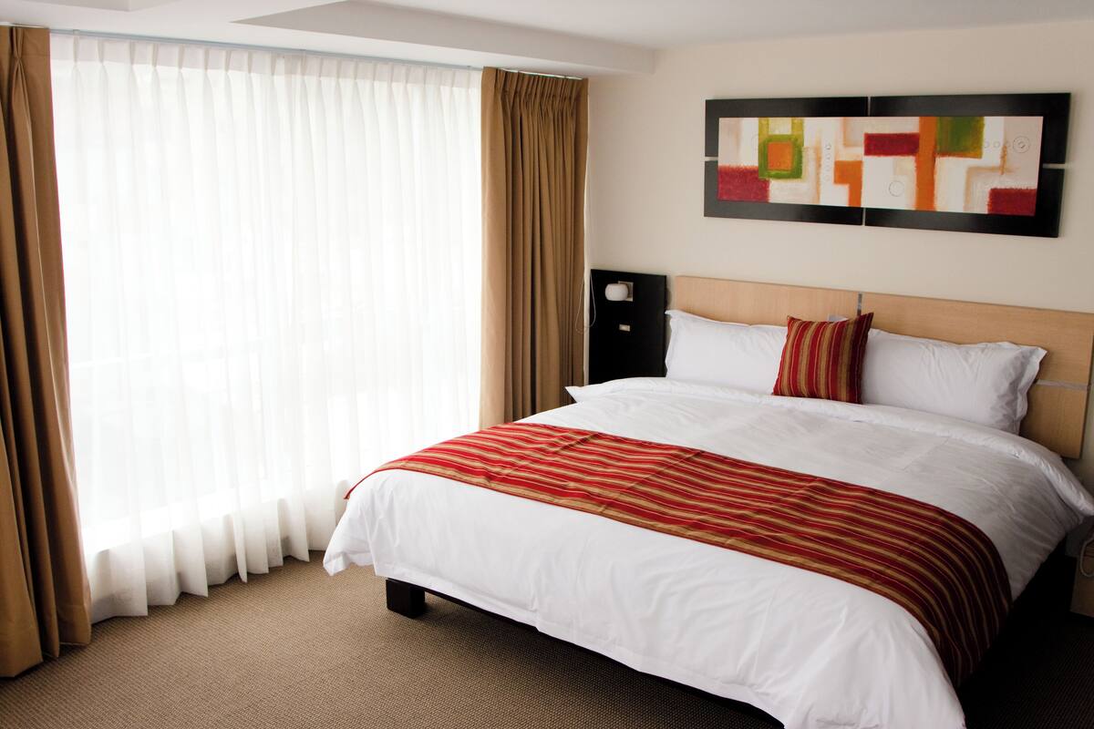 A hotel room with a large bed, a headboard, a wall-mounted artwork, and a window with curtains.