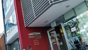A hotel entrance with steps leading up to a glass door, a sign for Allpa Hotel & Suites, and a person with a suitcase. - Allpa Hotel & Suites (Lima)
