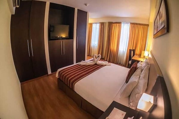 Ett hotellrum med en stor säng, en garderob, en tv och ett skrivbord med en lampa.