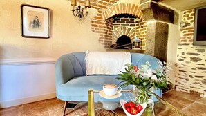 A cozy living room with a blue sofa, a small table with a cup of coffee, a vase with flowers, and a brick fireplace.