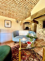 Una sala de estar acogedora con un sofá azul, una mesita con una taza de café, un jarrón con flores y una chimenea de ladrillo.