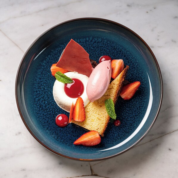 A dessert on a blue plate with strawberries, a cherry, and mint leaves. - Château d'Apigné (Le Rheu)