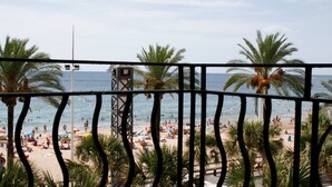 Vista a la playa desde un balcón, con palmeras y una torre de salvavidas.