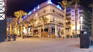 Un hotel con fachada blanca, varios balcones y palmeras al frente.